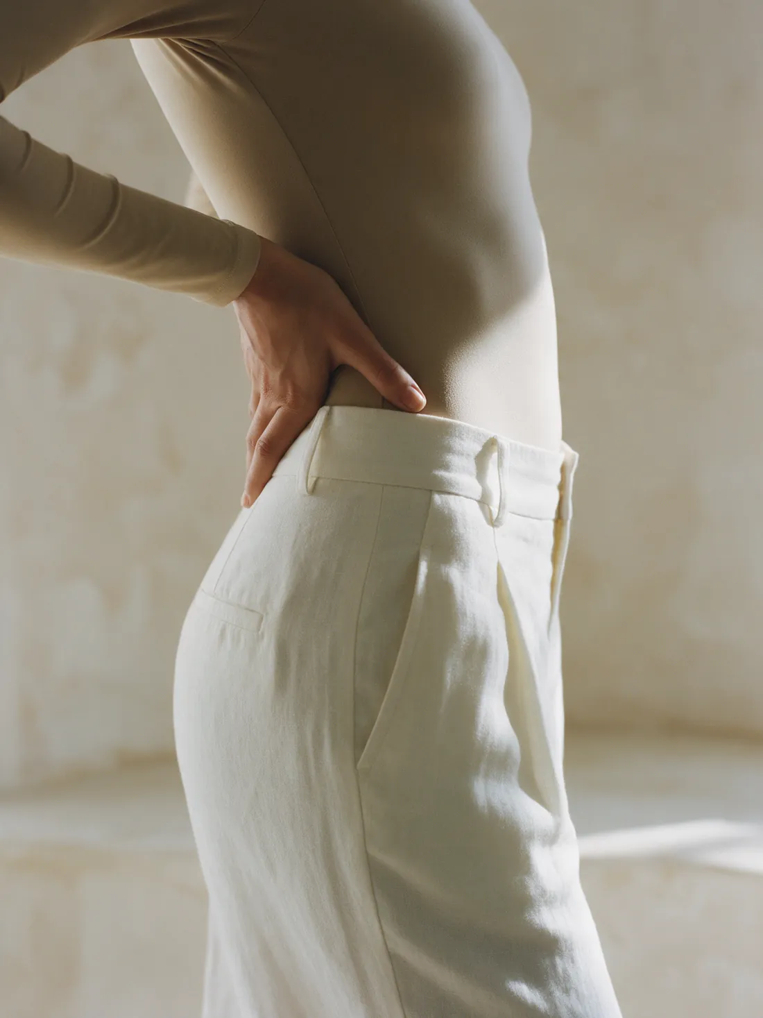 Silhueta de cintura feminina em body bege e calça de linho, em luz lateral